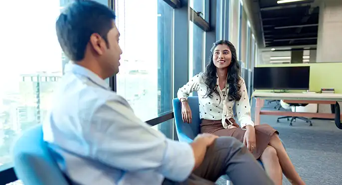 Two colleagues engaged in conversation by a window.