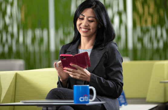asian female employee sitting with a coffee and smiling at her phone