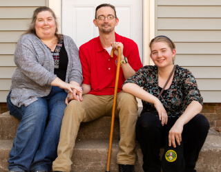 veteran with a cane sitting in front of a house with his wife and daughter