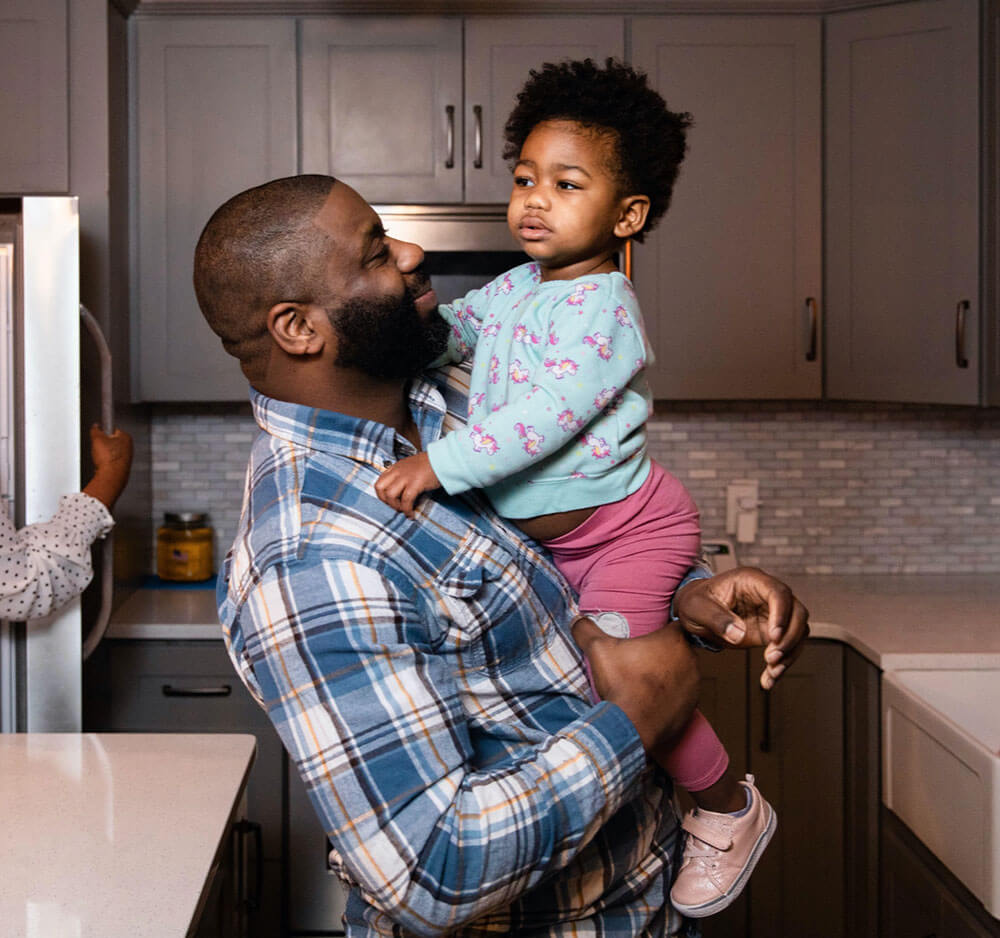 Black male employee holding his young child at home