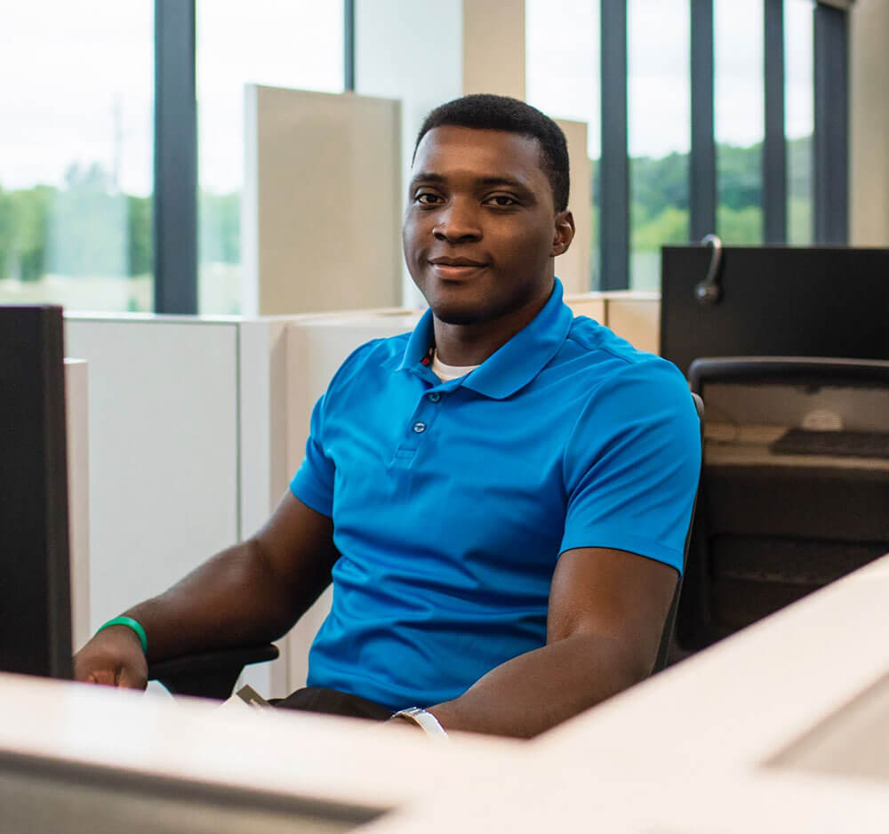 young black employee in a polo shirt, sitting at a desk in front of a computer