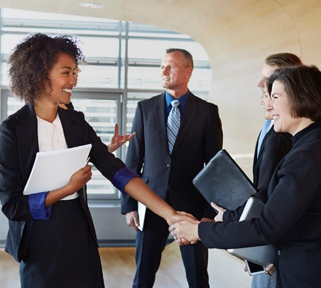 black female employee in a business suit shaking hands with a group of clients in a sunlit conference room