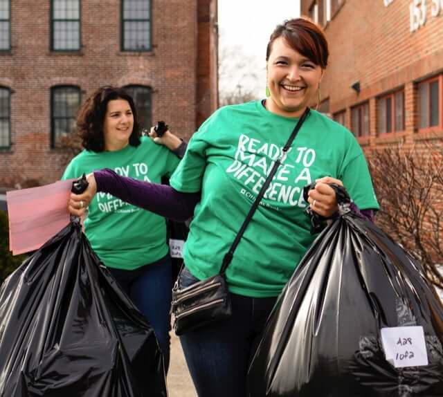 2 female employees wearing green 'ready to make a difference' t-shirts and carrying large trash bags