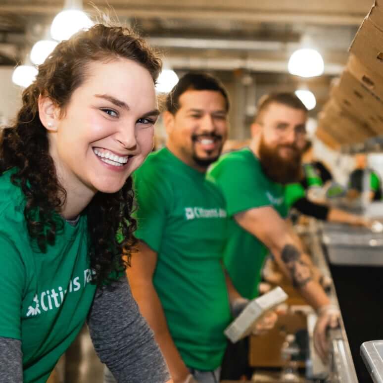 3 smiling employees wearing green Citizens t-shirts while volunteering in a community kitchen