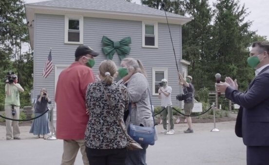 a family arriving at a newly constructed house with a camera crew in the background