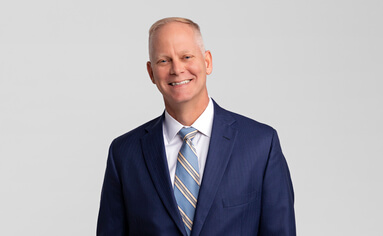 older male wearing a navy blue suit and tie and smiling