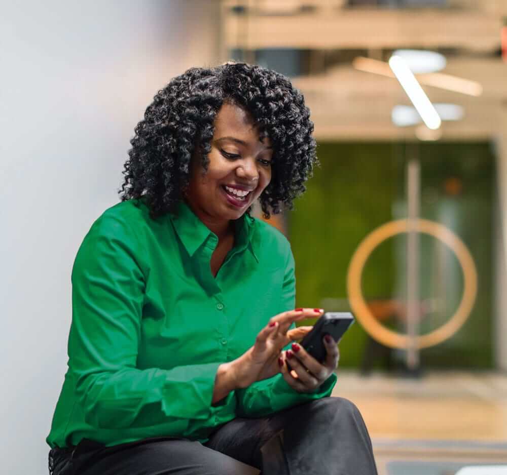 black female employee sitting and smiling while she looks at her phone