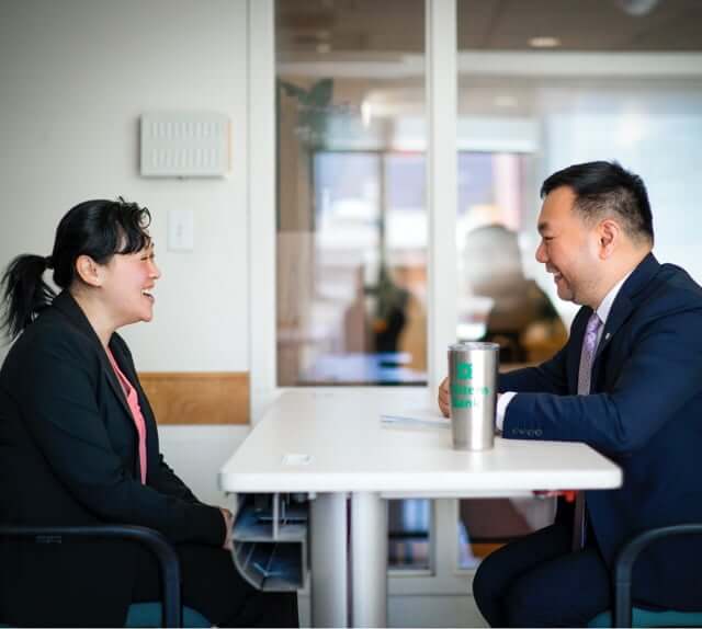 asian male and asian female employee wearing business suits and chatting at a table over coffee