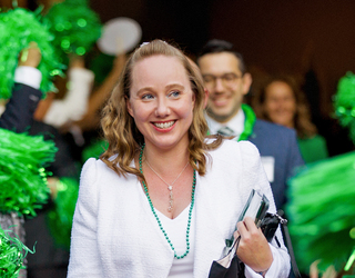 smiling female employee being celebrated by coworkers waving green pom-poms