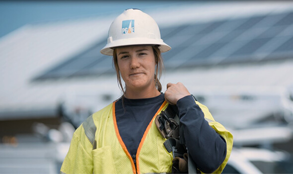 Lineworker woman is posing while wearing hardhat and gear.