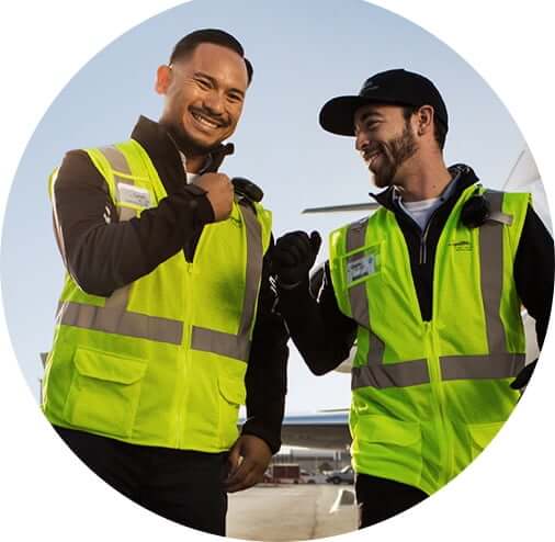 two male line service technicians smiling and bumping fists on a tarmac