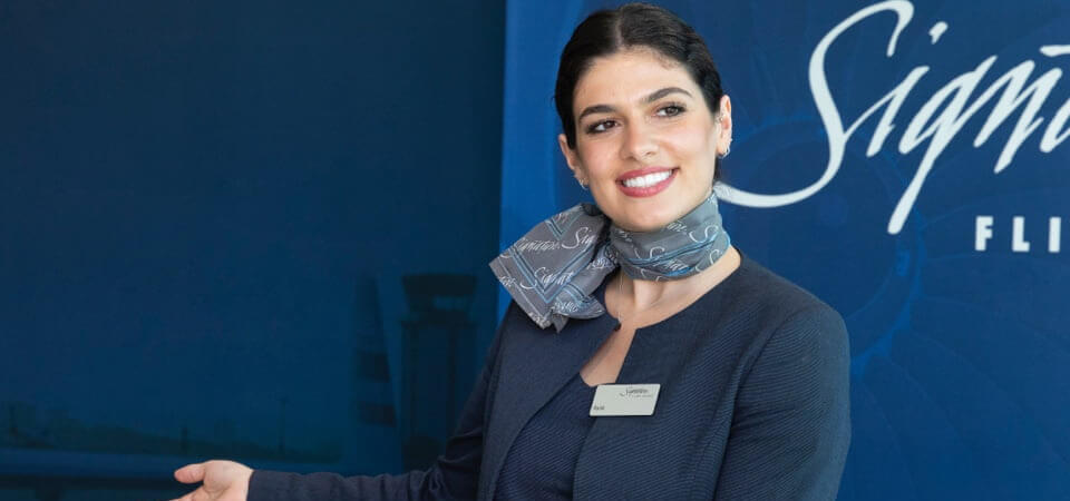 friendly female customer service representative motioning for passengers to board a plane