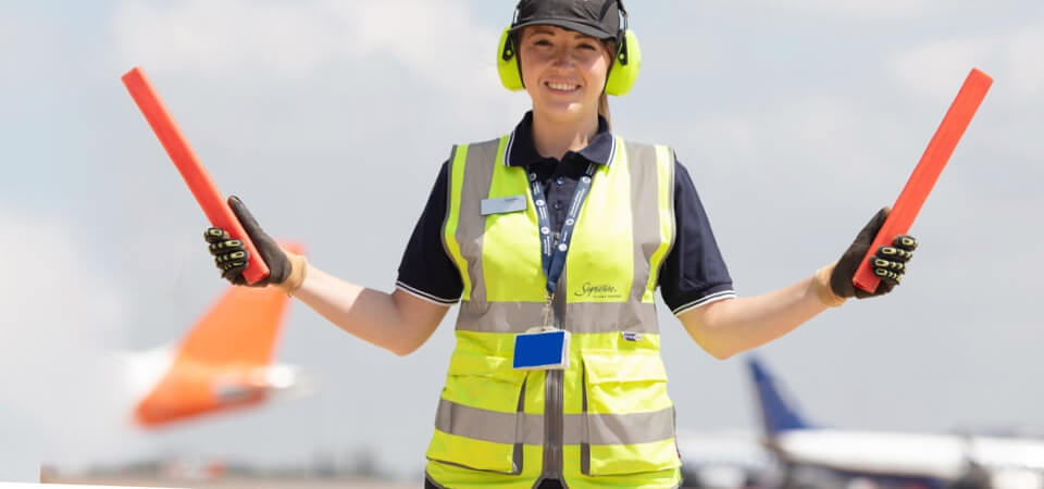 female line service technician in a reflective vest directing plane traffic