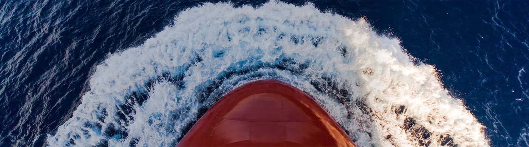 The stern of a shipping vessel, creating a wake as it moves through the ocean.