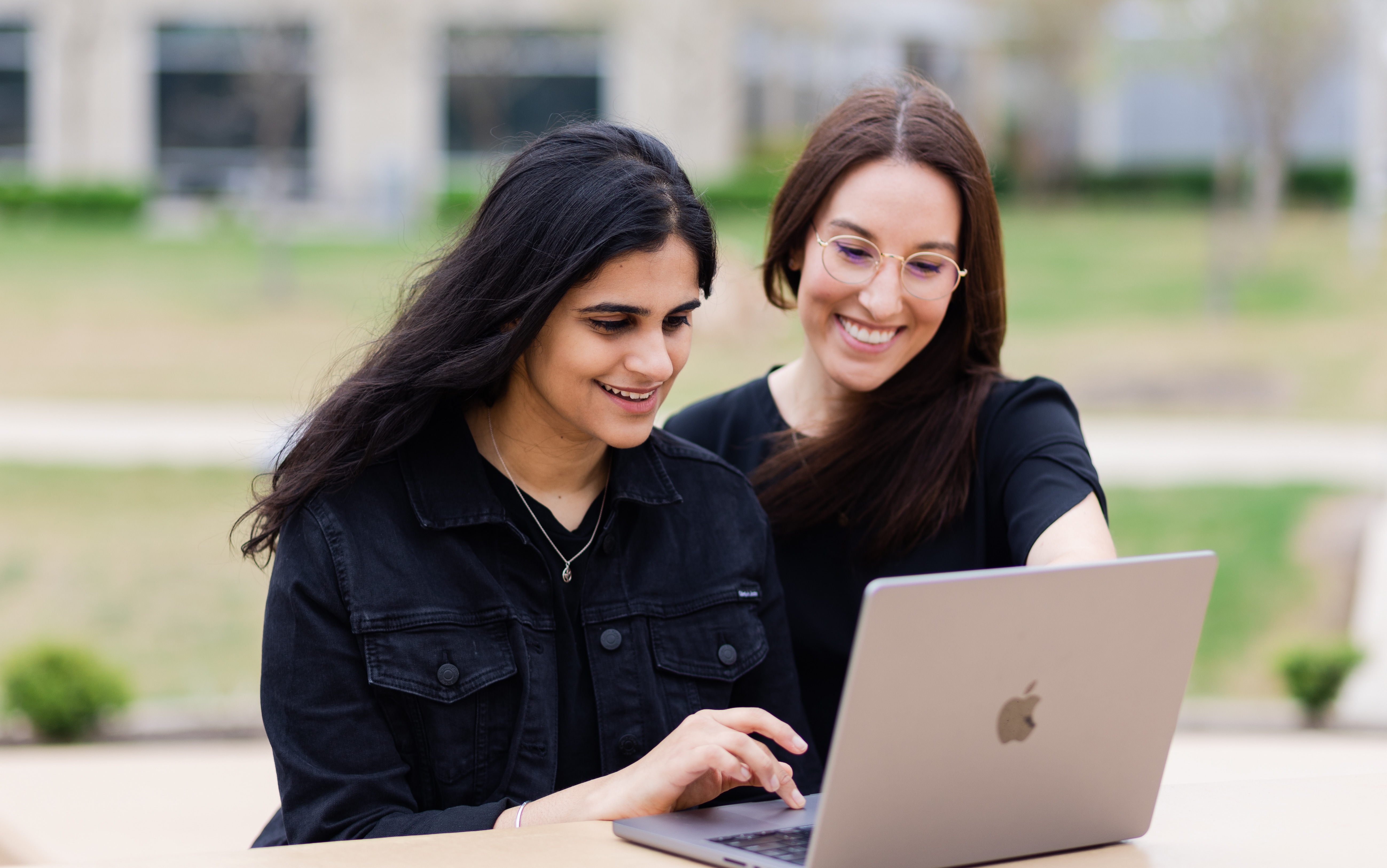 Two people using laptop together outdoors at table