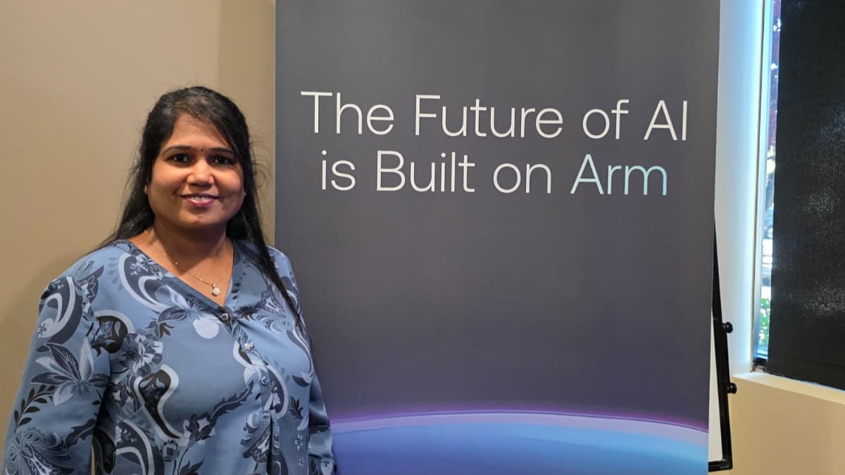 Manjula stands by a banner that reads "the future of AI is built on Arm"
