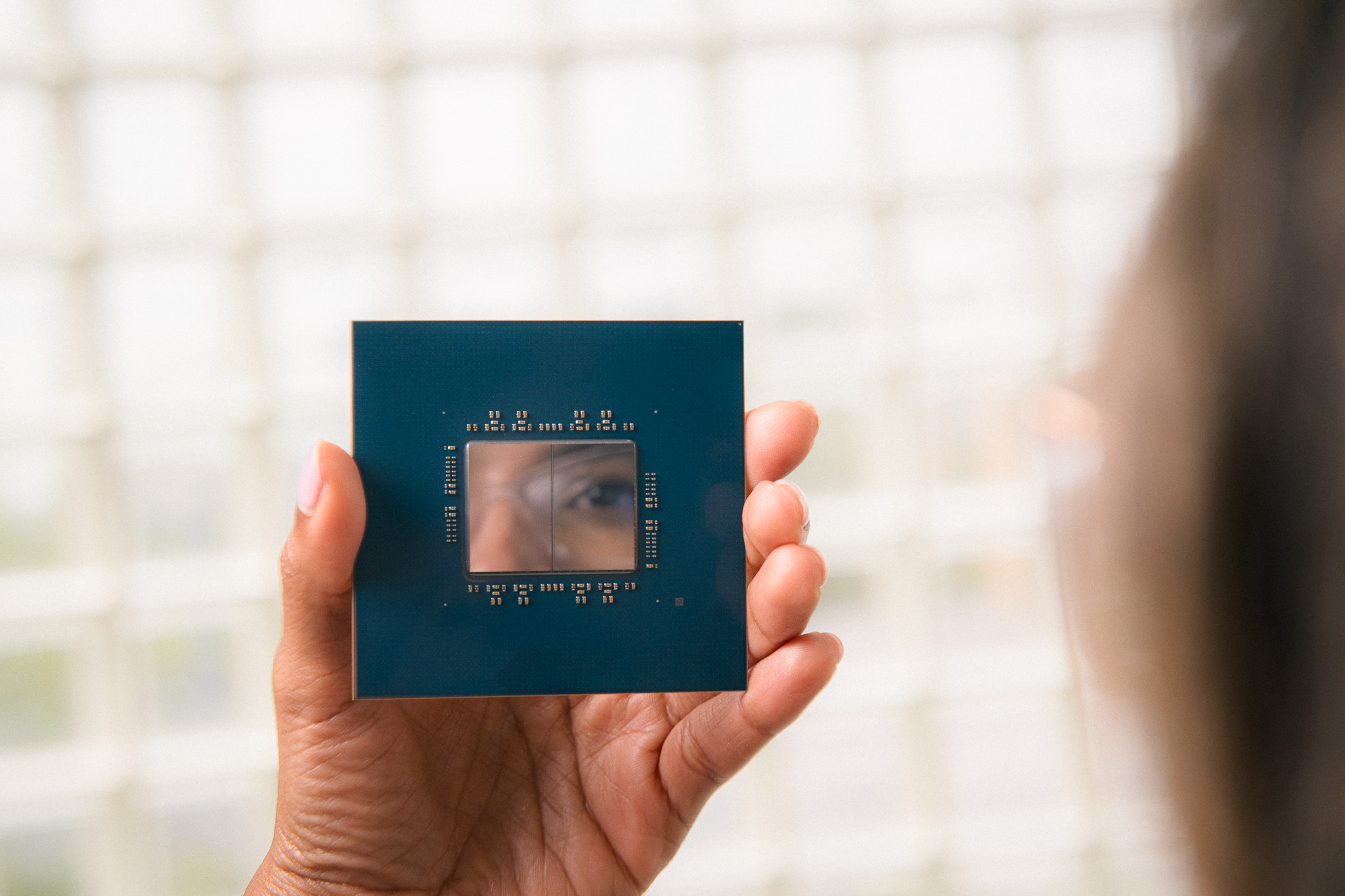 Person holding a semiconductor chip with its reflective surface showing their eye.