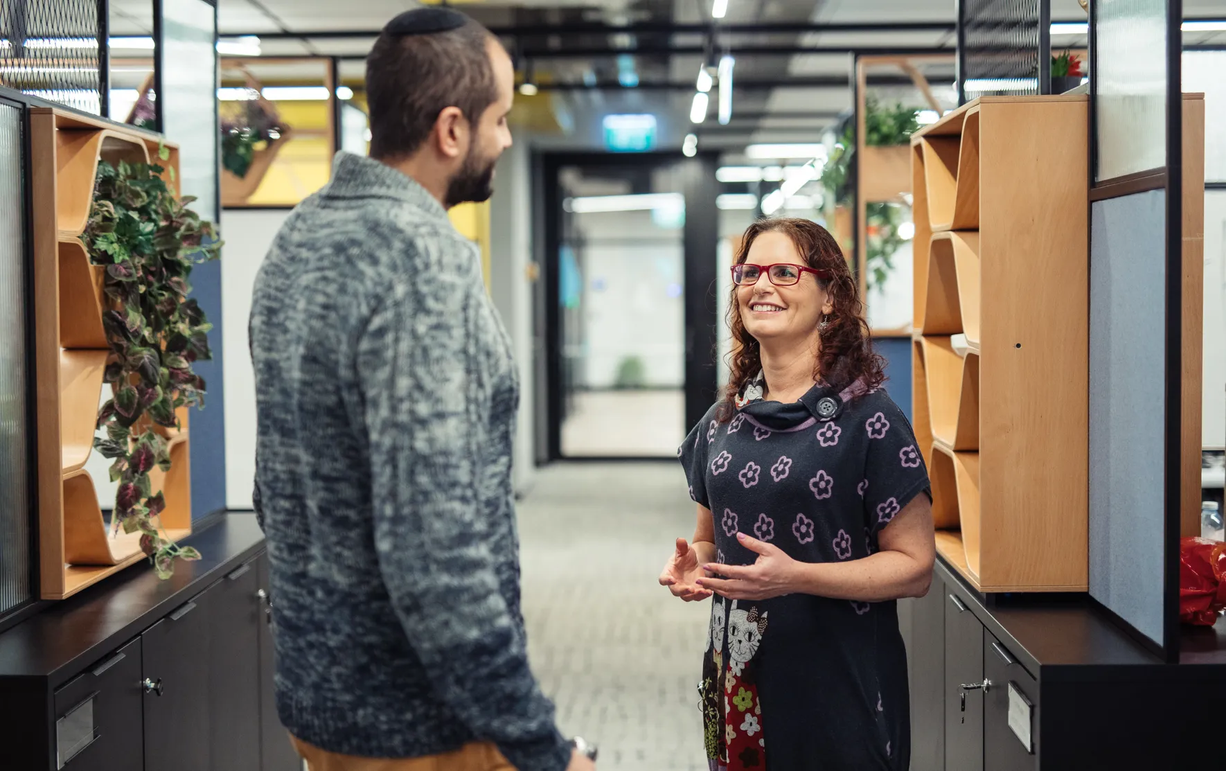 Two people talking in a modern office hallway.