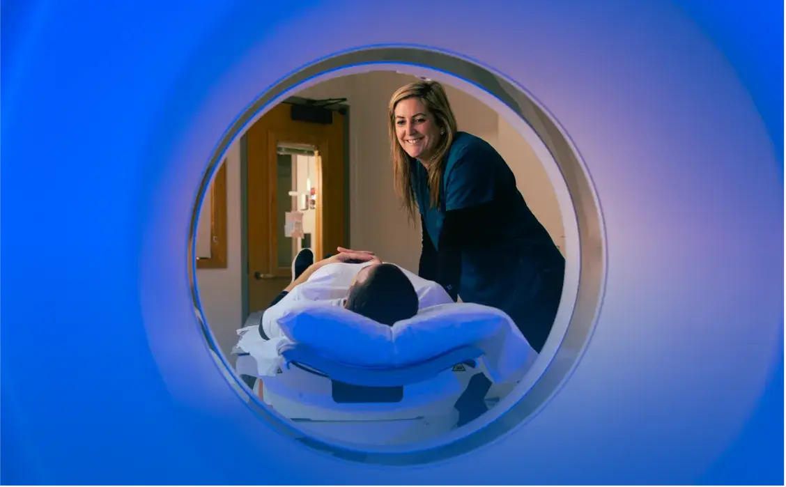 Female employee talking with a patient as the patient lays on a radiology imaging bed