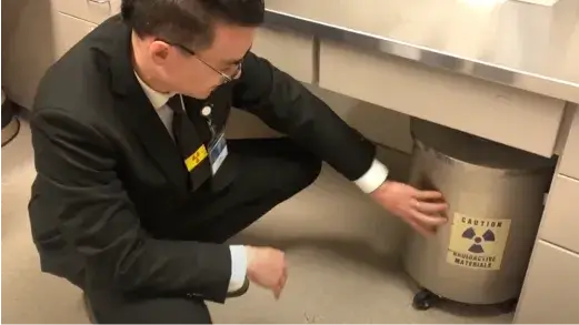 A Nuclear Medicine Technologist VCT looking at a container which seems to have what looks like a biohazard sticker on it (Video)