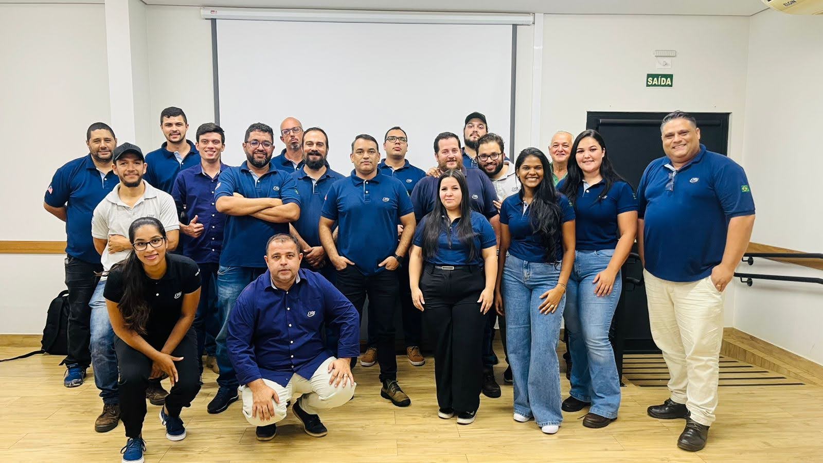 Team of employees posing together in a meeting room wearing blue shirts.