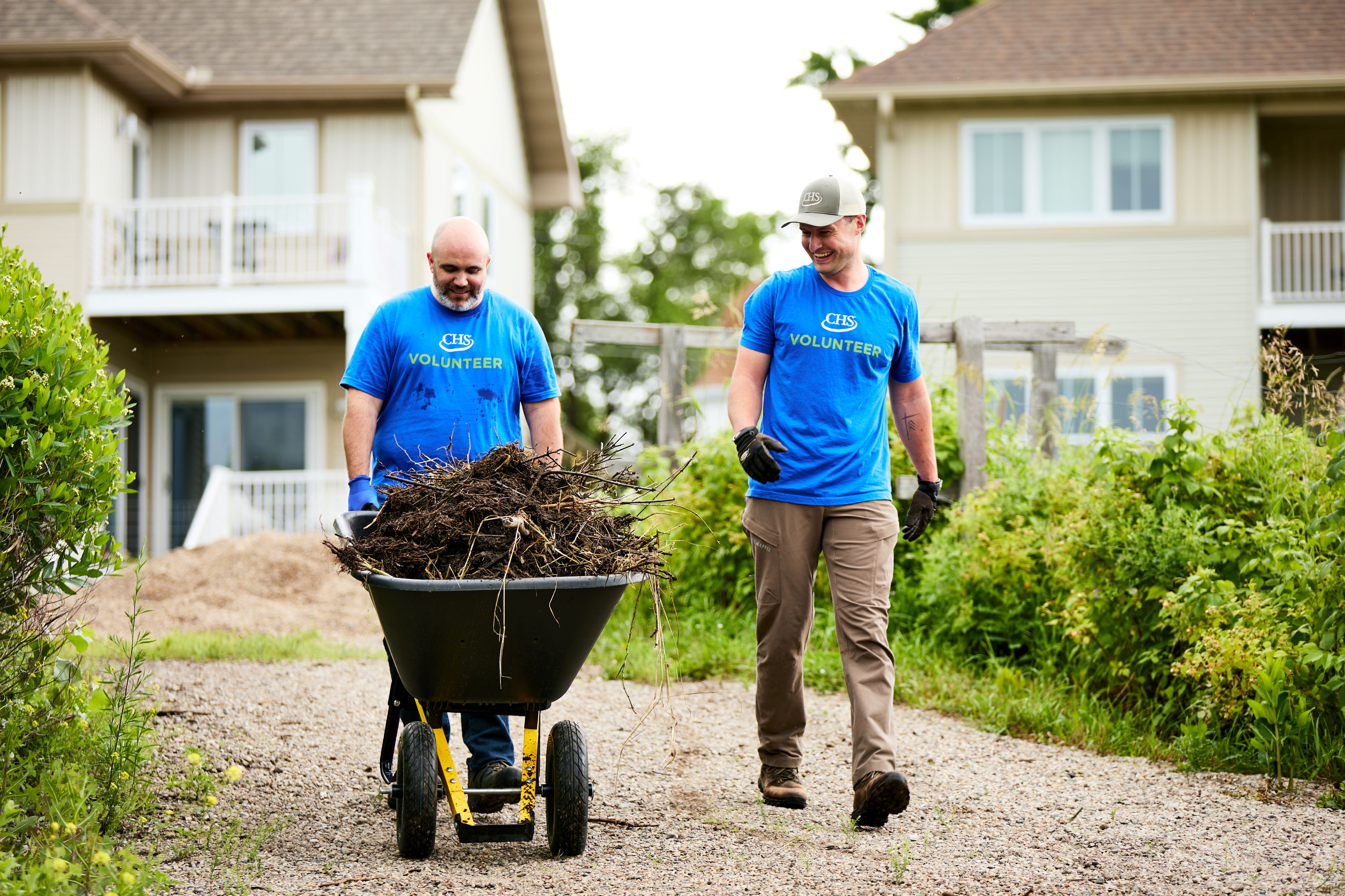 Two employees volunteering while pushing a wheelbarrow.