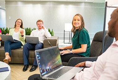 Interns on laptops talking in office
