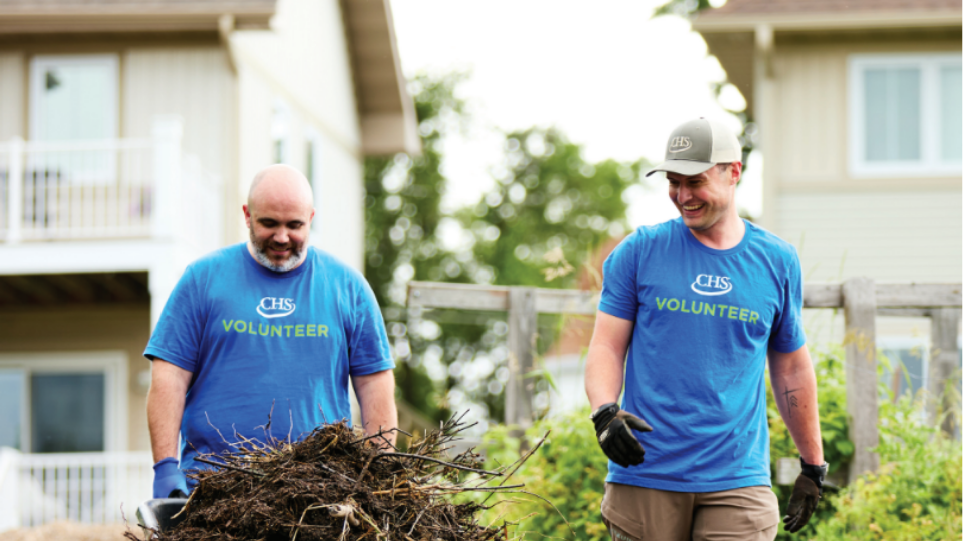 Two employees volunteering while pushing a wheelbarrow.