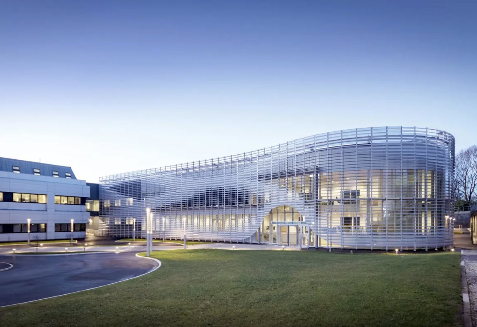 Modern exterior of Unilever's Port Sunlight office building, featuring a curved facade with metal lattice structure and large windows, set against a clear sky.