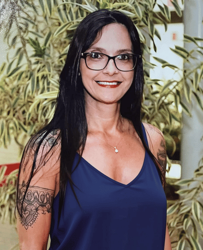 Jaqueline é uma mulher branca de cabelos castanhos longos. Está sorrindo e usa um óculos de armação marrom e uma camiseta polo na cor roxa, com o logo da Unilever