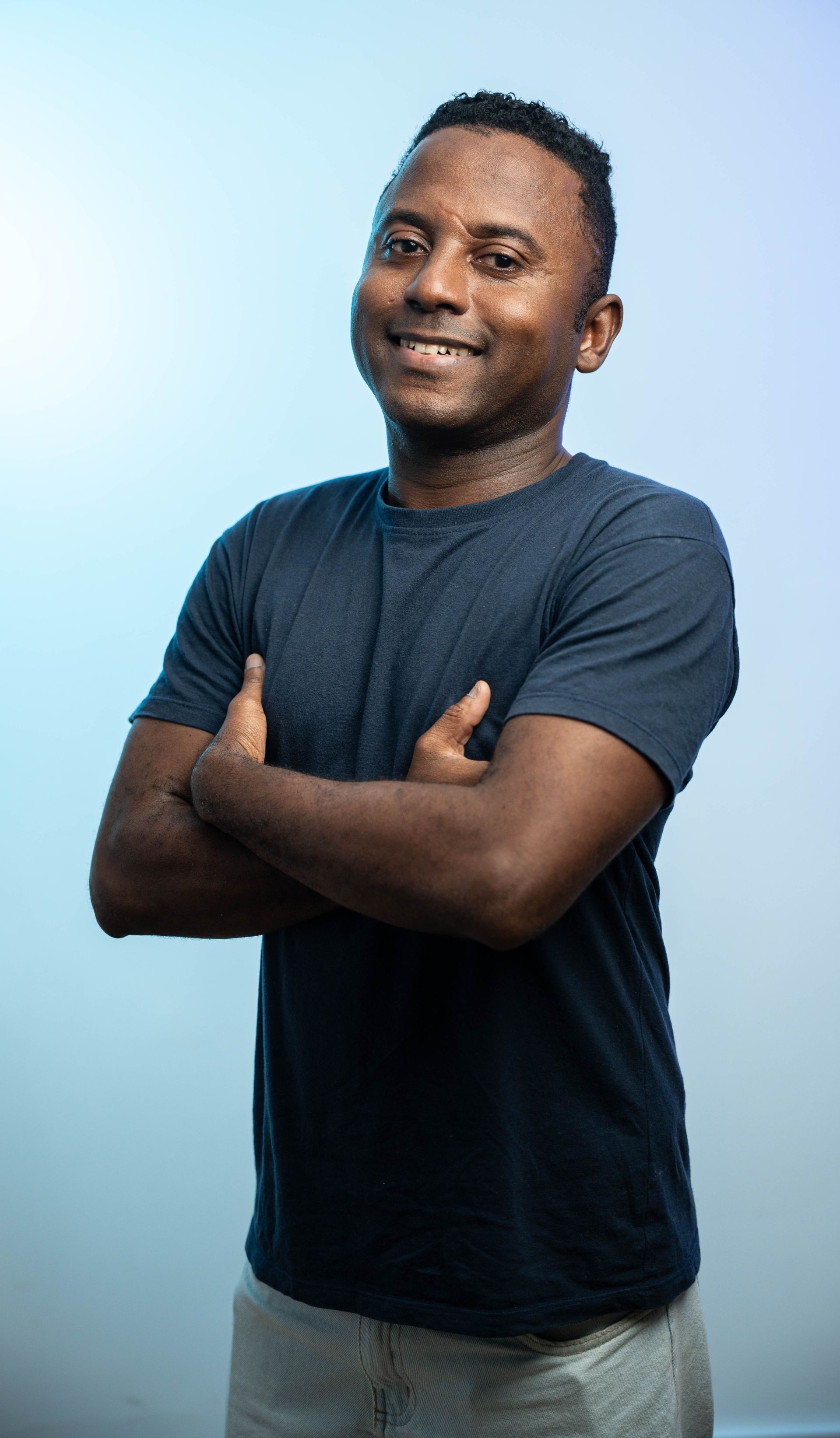 Homem sorrindo pousa para a foto de braços cruzados com uma expressão de autoconfiança