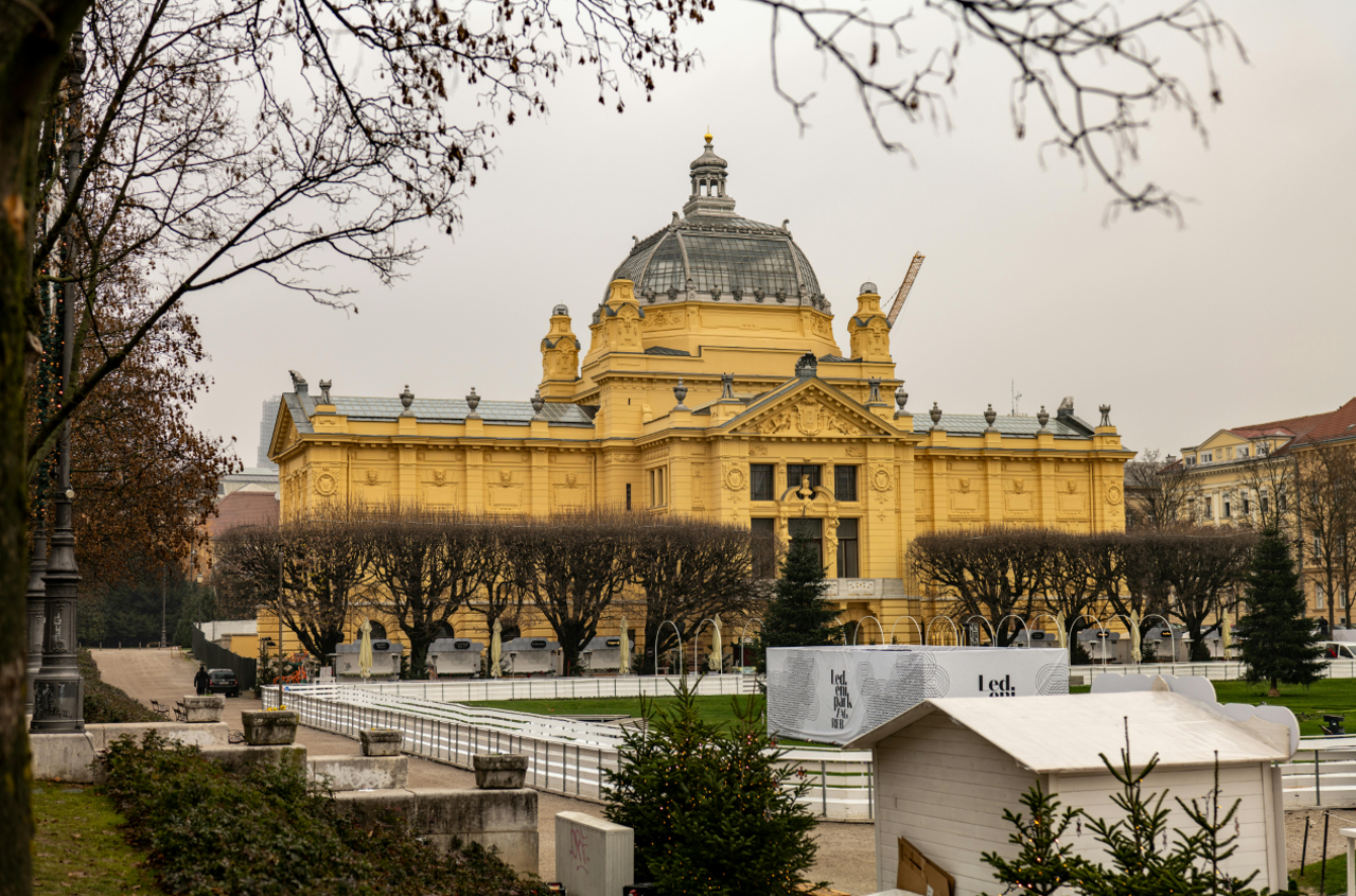 Historic yellow exhibition building with a domed roof surrounded by trees on an overcast day.