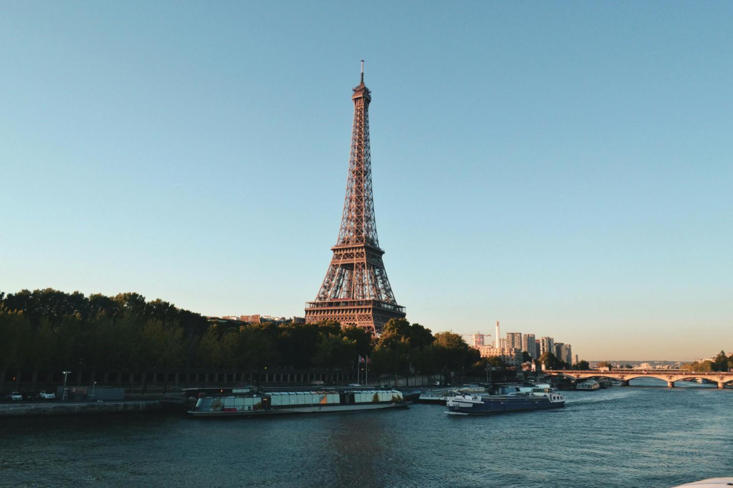 Eiffel Tower by the river under clear blue sky.