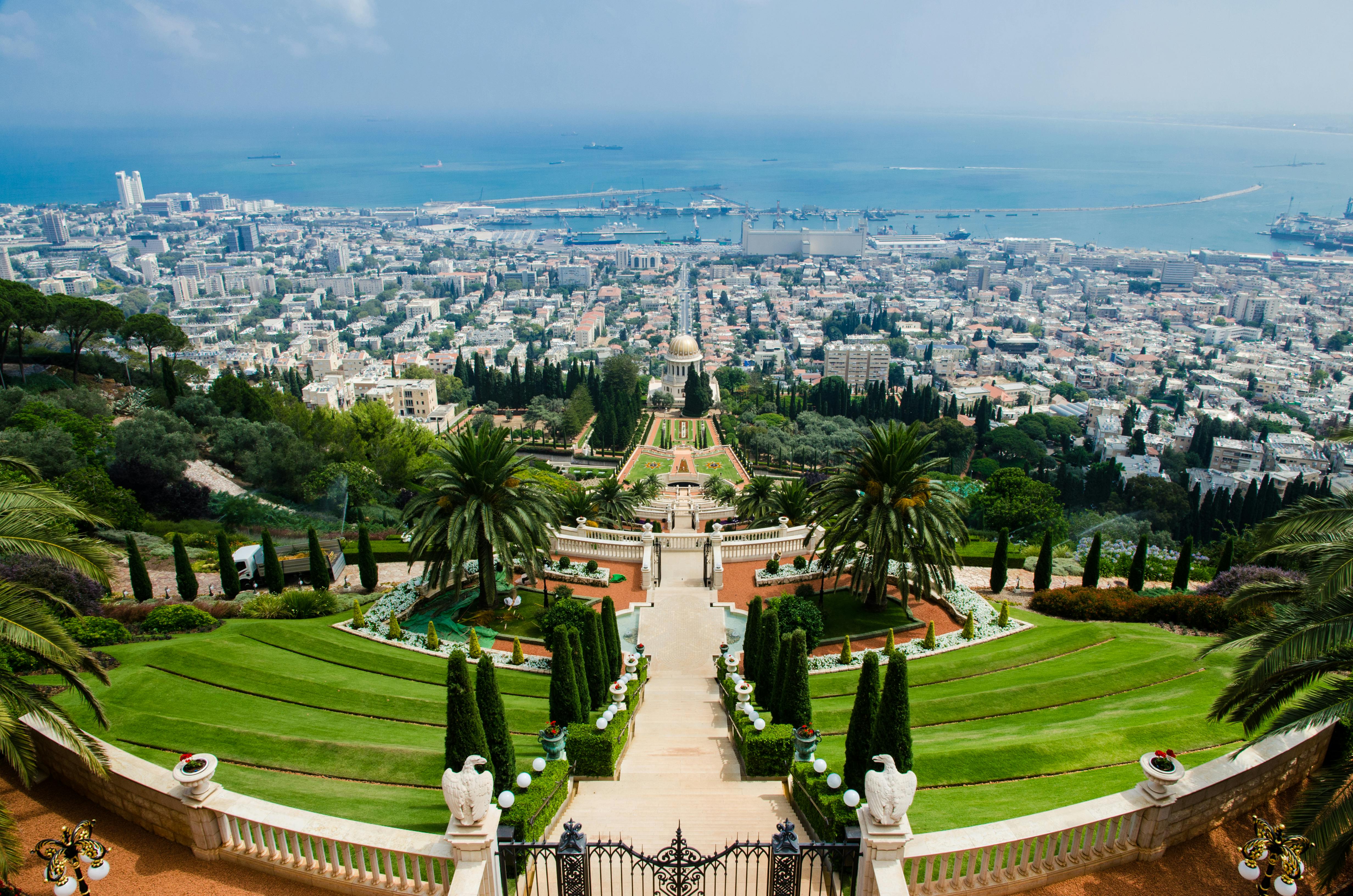 Elevated view of terraced gardens leading down to a coastal city and the sea in the background.