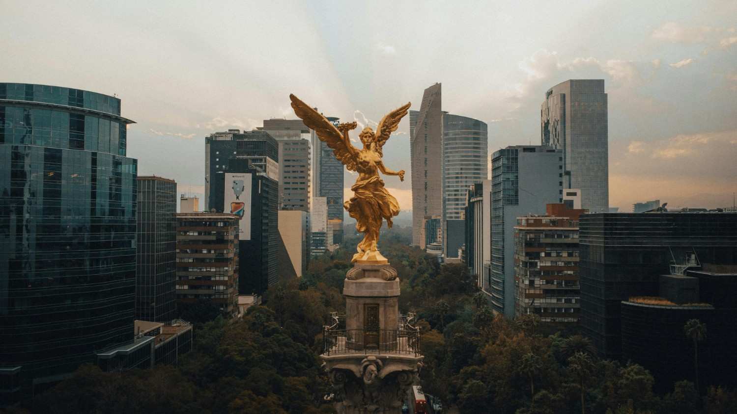 Golden angel statue amid tall modern city buildings
