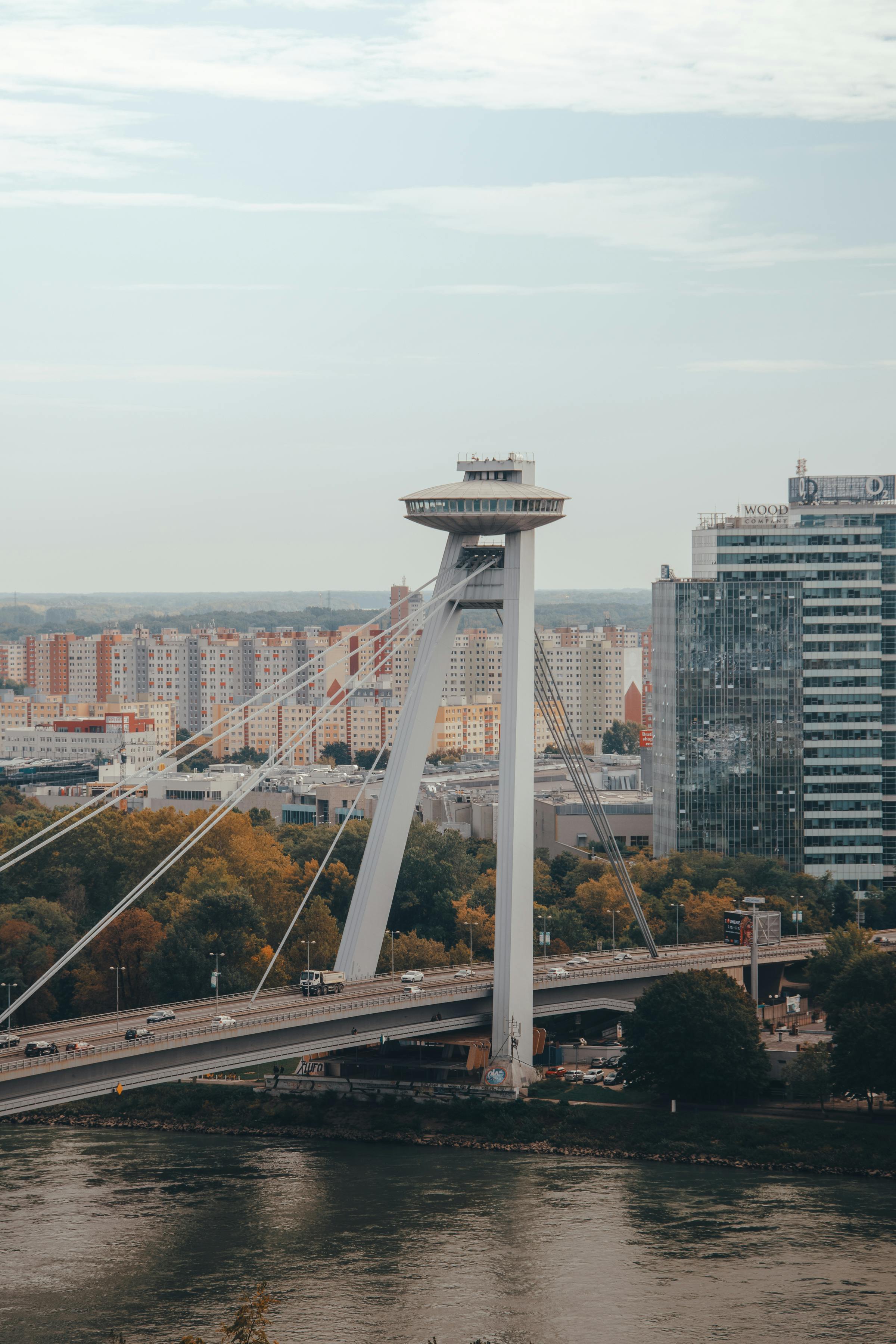 View of a modern cable‑stayed bridge with a distinctive tower and surrounding city buildings by the river.