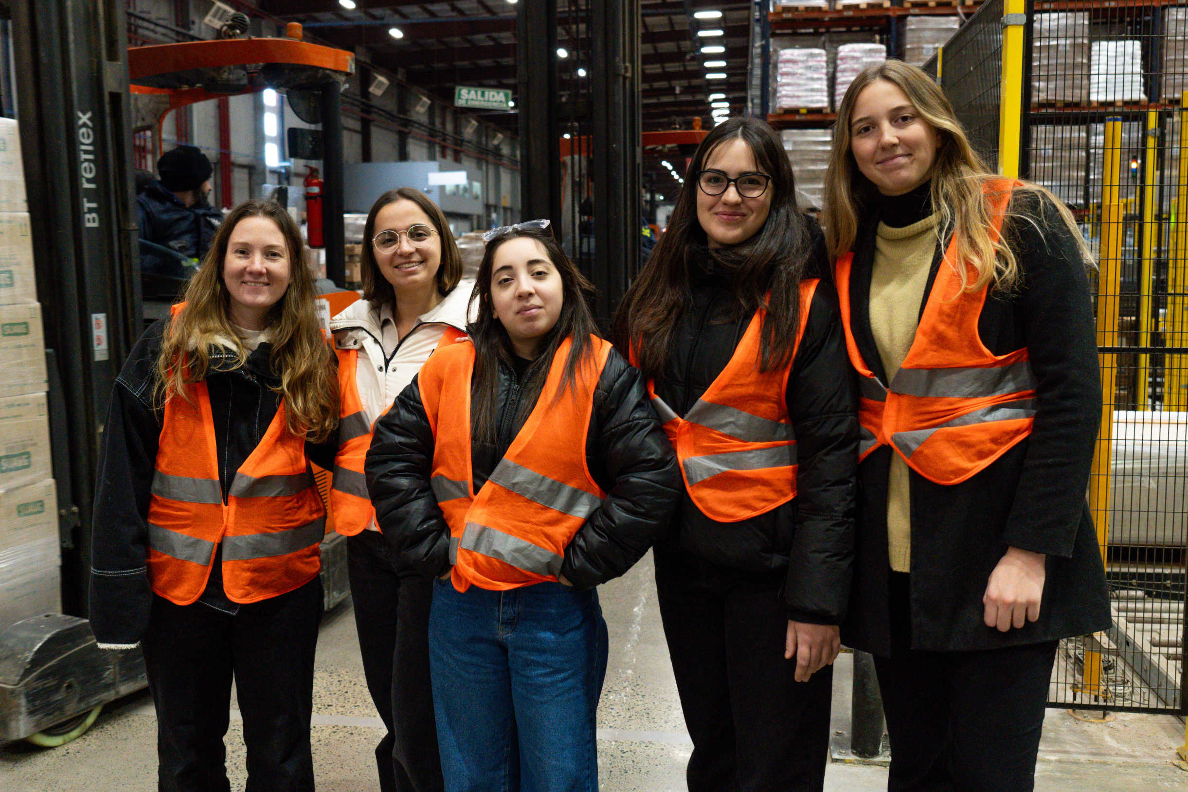 Workers wearing orange safety vests inside a warehouse.
