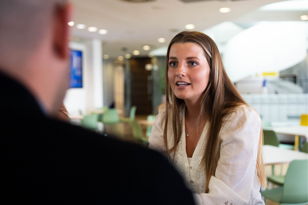 Two people in conversation at a table in a modern office environment.