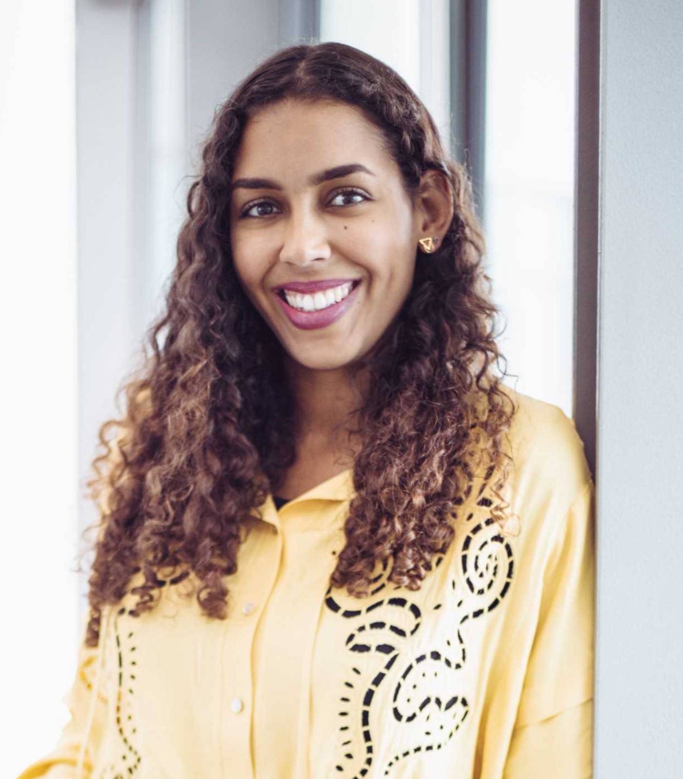 Smiling woman with curly hair in a yellow shirt.