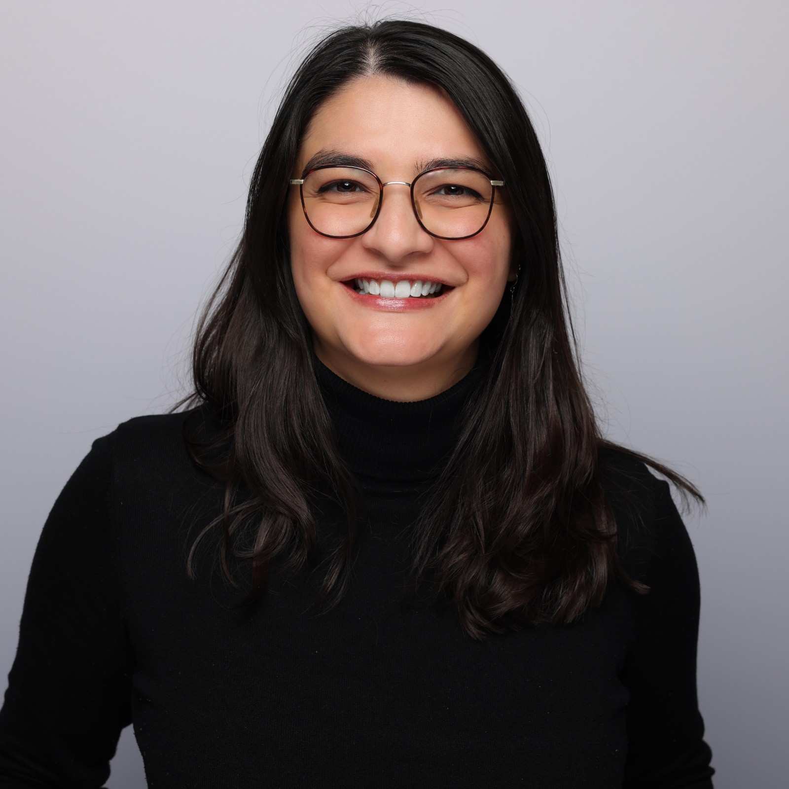 Smiling woman in glasses and a black turtleneck.