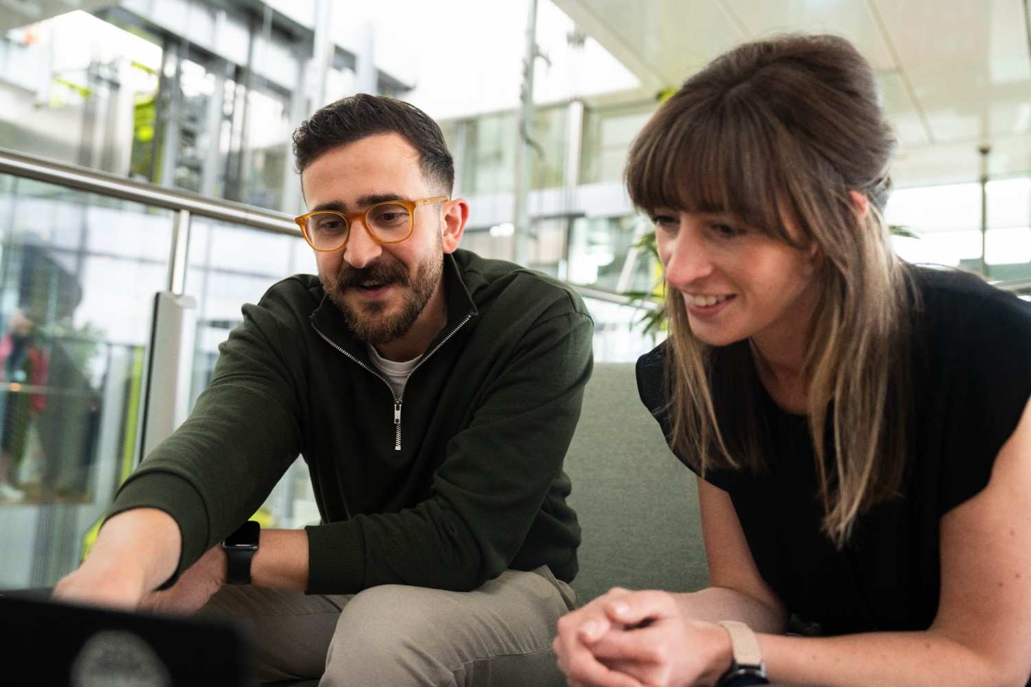 Two colleagues smiling and discussing something on a laptop.