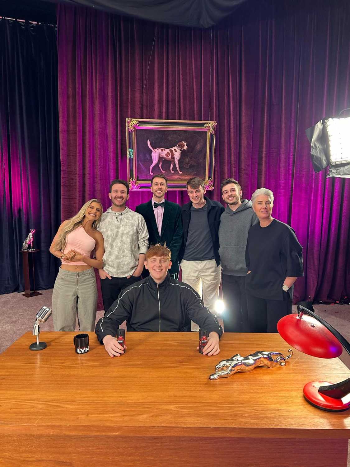 The team on a Lynx (Axe) branded studio set during a content shoot, seated and standing around a podcast desk.