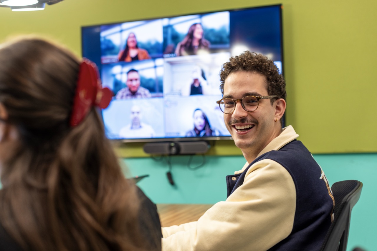 A colleague smiles during a video meeting in a Unilever office, with other team members visible on a screen in the background