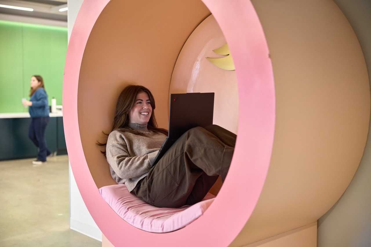 Employee using a laptop while seated in a comfortable workspace pod.