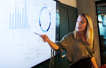 Frau, die während einer Präsentation auf einen Bildschirm hinter ihr zeigt