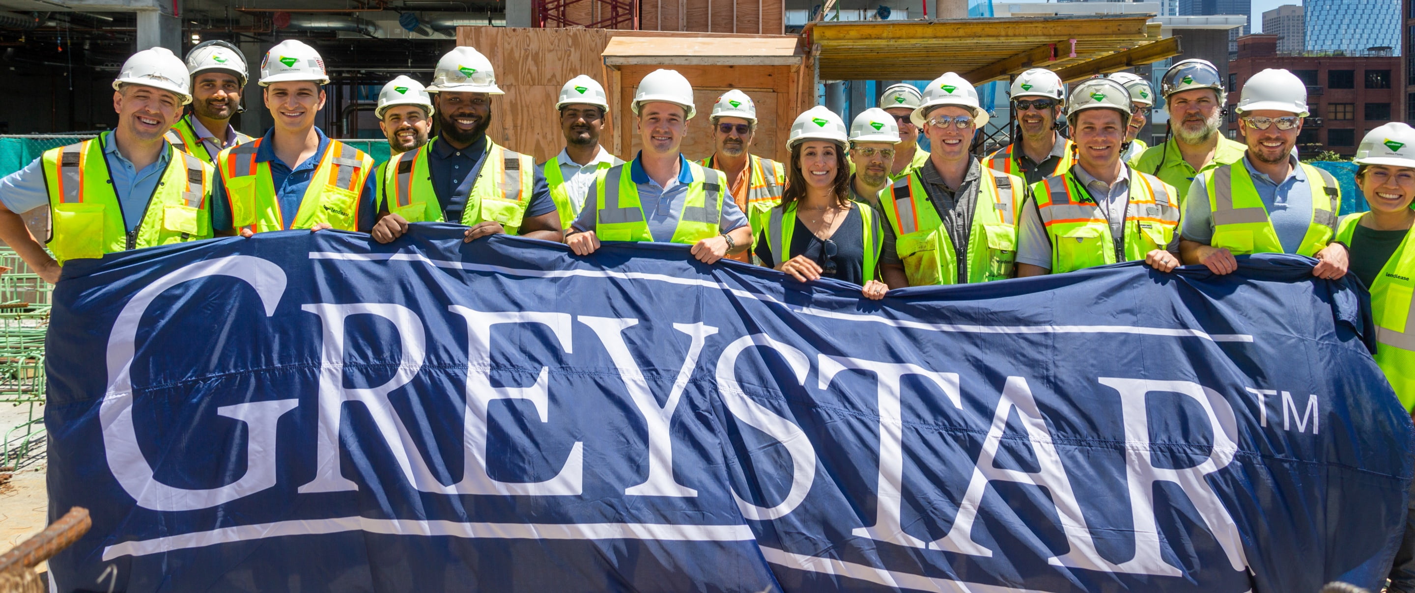 Group of construction workers holding a Greystar banner, smiling for a picture