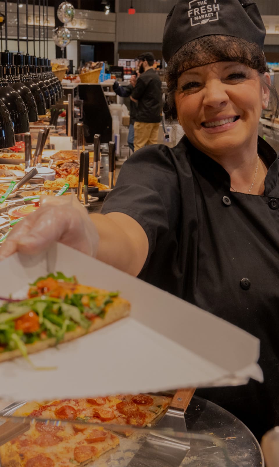 Young woman, wearing black facemask, white shirt and blue apron, loading groceries into shopping cart.