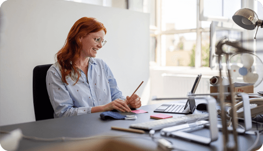 Employee smiling towards laptop while writing down notes