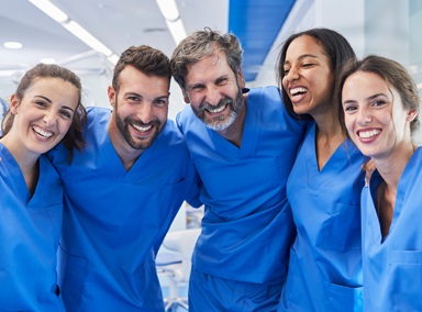 Ein Team medizinischer Pfleger und Pflegerinnen schaut lächelnd in die Kamera.