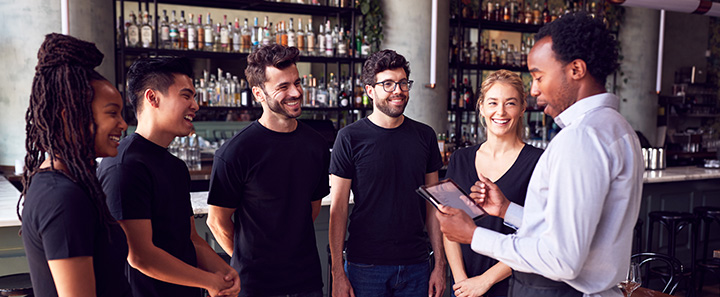 Guy in button up shirt talking to 4 others wearing black t-shirts
